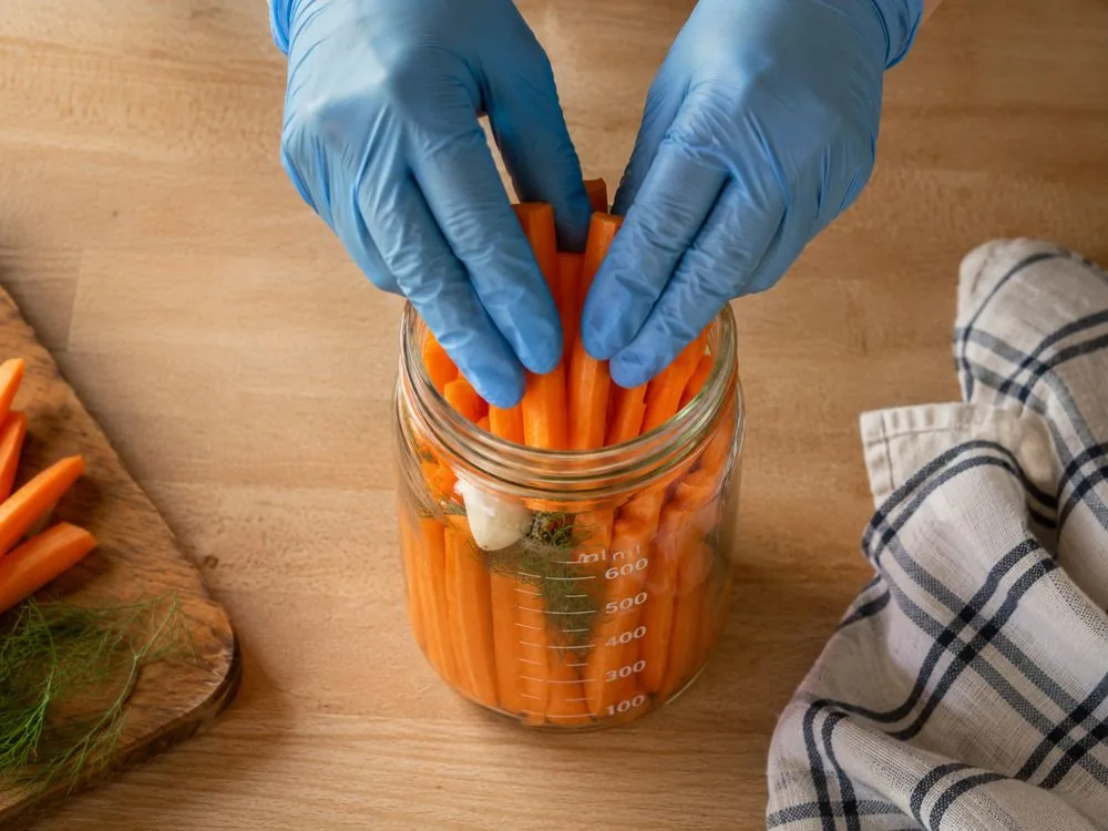 Tassage des bâtonnets de carottes dans le bocal gradué avec ail et aneth